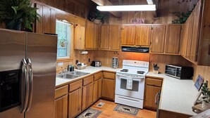 A cabin-style kitchen with wooden cabinets, a stainless steel refrigerator, a stove, and a microwave. - Bigfoot's River Retreat (Mineral Bluff)