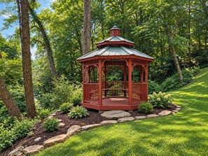 Um gazebo vermelho com cobertura de metal, rodeado por um jardim bem cuidado com grama, pedras e diversas plantas.