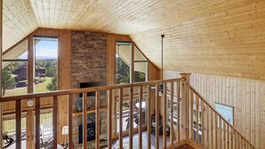 Une chambre spacieuse aménagée en loft, avec un plafond haut, de grandes fenêtres et une cheminée en pierre.
