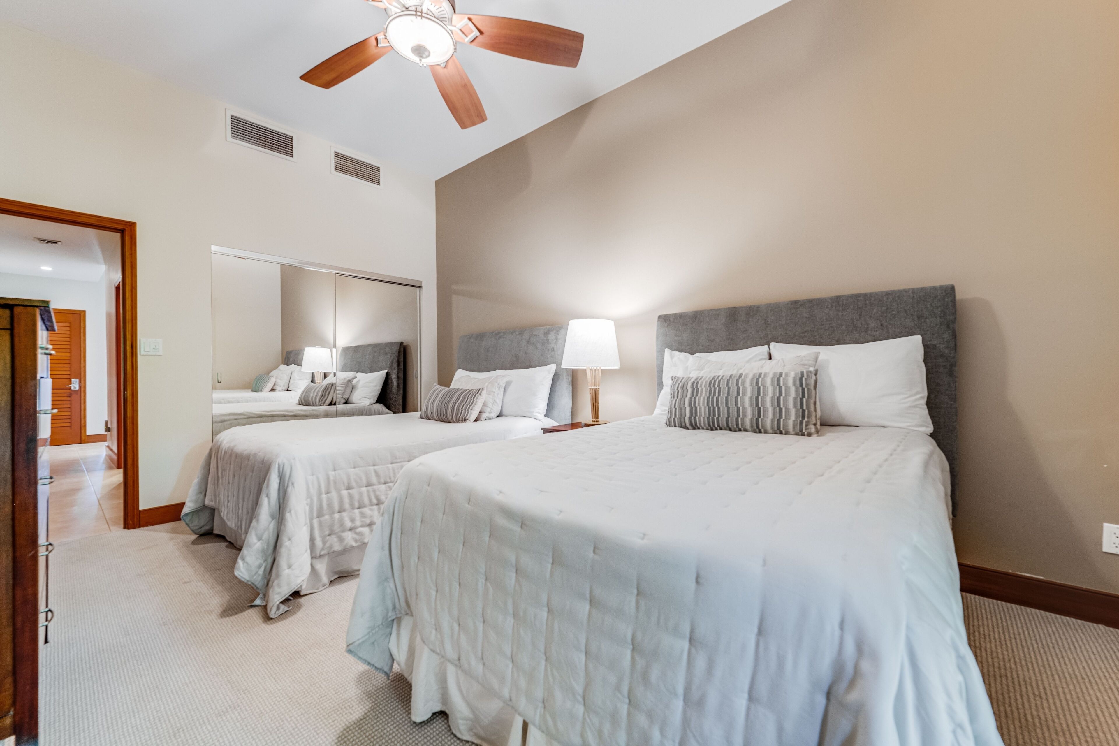 A hotel room with two beds, a ceiling fan, and a large mirror.