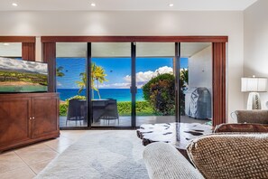 A room with a large sliding glass door leading to a balcony with a view of the ocean.