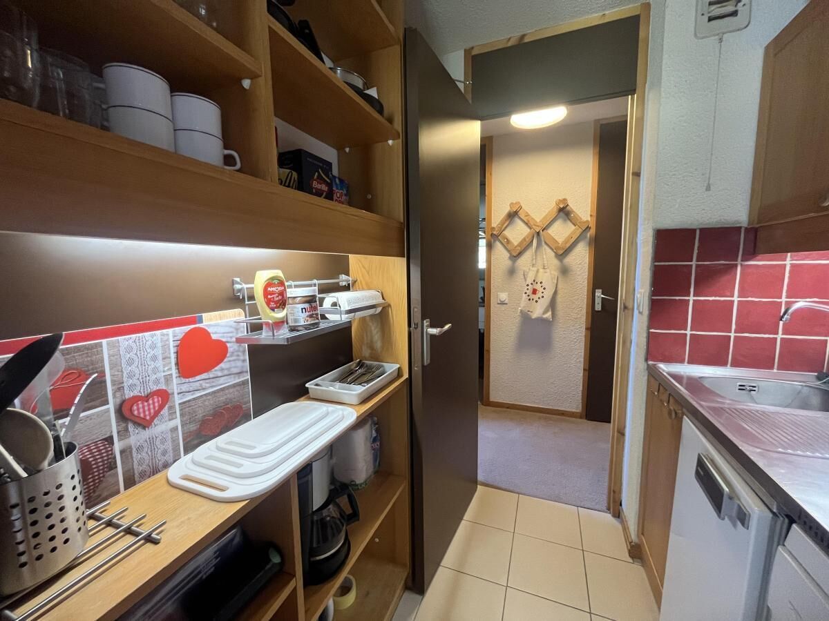 A compact kitchen with wooden shelves, a white countertop, and a red tiled backsplash.