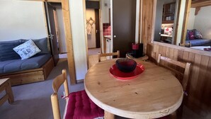 Et hyggeligt værelse med et træspisebord, en sofa og et køkken, der kan ses igennem en åben dør.