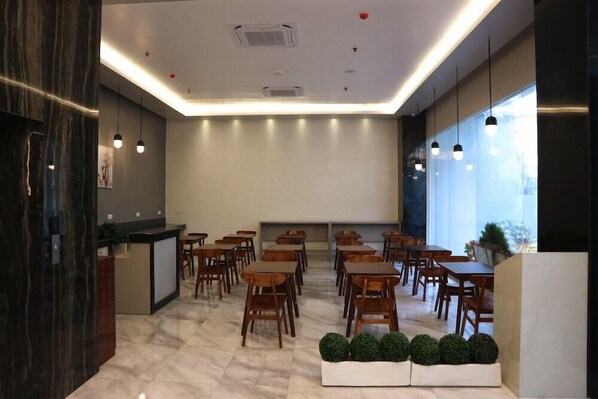 A modern dining area with marble flooring, wooden tables and chairs, a reception desk, and large windows allowing natural light. - Grand Thamrin Hotel (Jakarta)