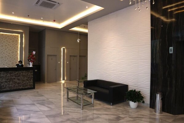 A modern lobby with a reception desk, a glass coffee table, a black sofa, and a textured wall. - Grand Thamrin Hotel (Jakarta)