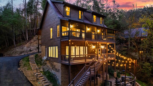 A two-story wooden cabin with multiple windows, a balcony, and a staircase leading to the upper level. - Best Family Cabin - Indoor Pool, Cinema, Arcade, Putt Putt, Spa, Fire Pit, Creek (Sevierville)