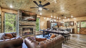 A spacious living area with a stone fireplace, leather sofas, and a dining area with a wooden table and chairs. - Best Family Cabin - Indoor Pool, Cinema, Arcade, Putt Putt, Spa, Fire Pit, Creek (Sevierville)