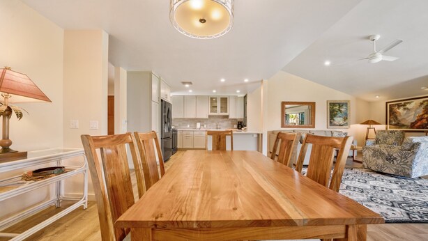 A spacious dining area with a wooden table and chairs, a kitchen in the background, and a ceiling fan. - Wailea Elua, #1104 2 Bedroom Condo by RedAwning (Kihei)