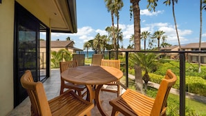 A balcony with a wooden table and chairs, overlooking a garden with palm trees and a clear sky. - Wailea Elua, #1104 2 Bedroom Condo by RedAwning (Kihei)