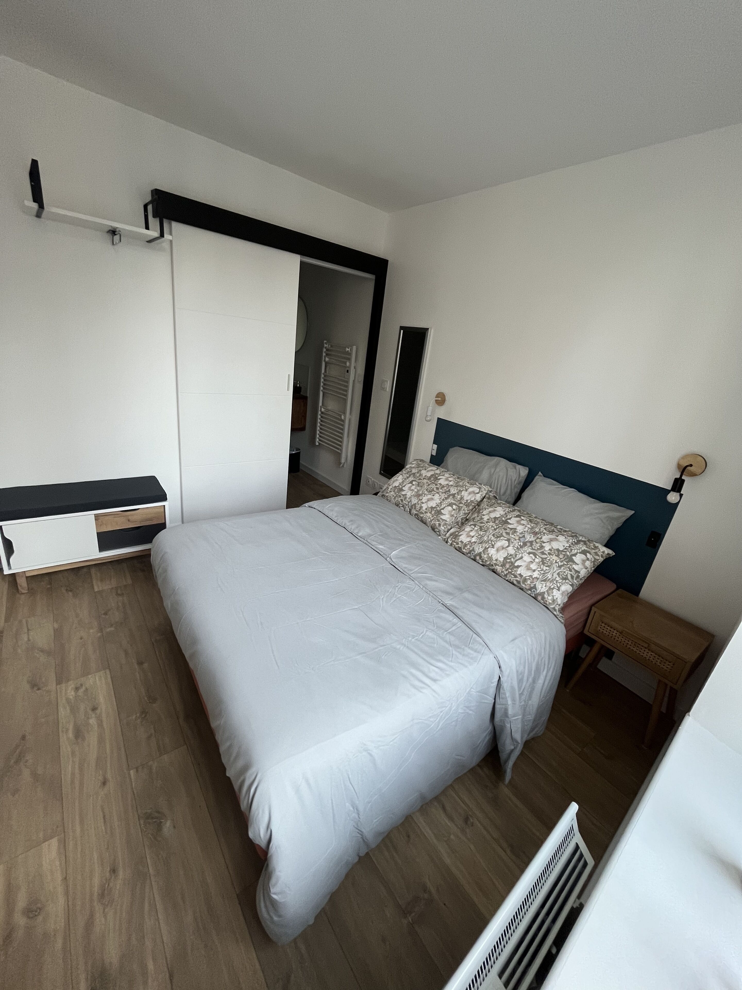 Ein Schlafzimmer mit Bett, Kleiderschrank, Heizkörper und Spiegel.