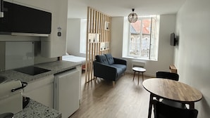Une cuisine moderne équipée d’un four à micro-ondes encastré, d’un petit réfrigérateur et d’un plan de travail en granit. On y trouve un coin repas avec une table ronde en bois et des chaises, ainsi qu’un canapé bleu à l’arrière-plan.