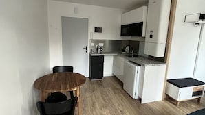Une cuisine compacte avec des appareils électroménagers blancs, une table à manger avec des chaises et un petit coin salon avec un canapé de couleur foncée.