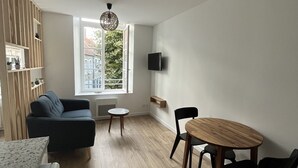 Un salon moderne comprenant un canapé, une table à manger avec des chaises, un téléviseur fixé au mur et une fenêtre donnant sur un paysage verdoyant.