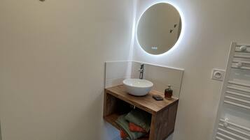 Een moderne badkamer met een houten wastafelmeubel, een ronde spiegel met verlichting, een witte wasbak en een handdoekrek.