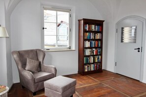 Cozy reading nook with a comfortable armchair and ottoman, wooden bookshelf, and a hinged door.