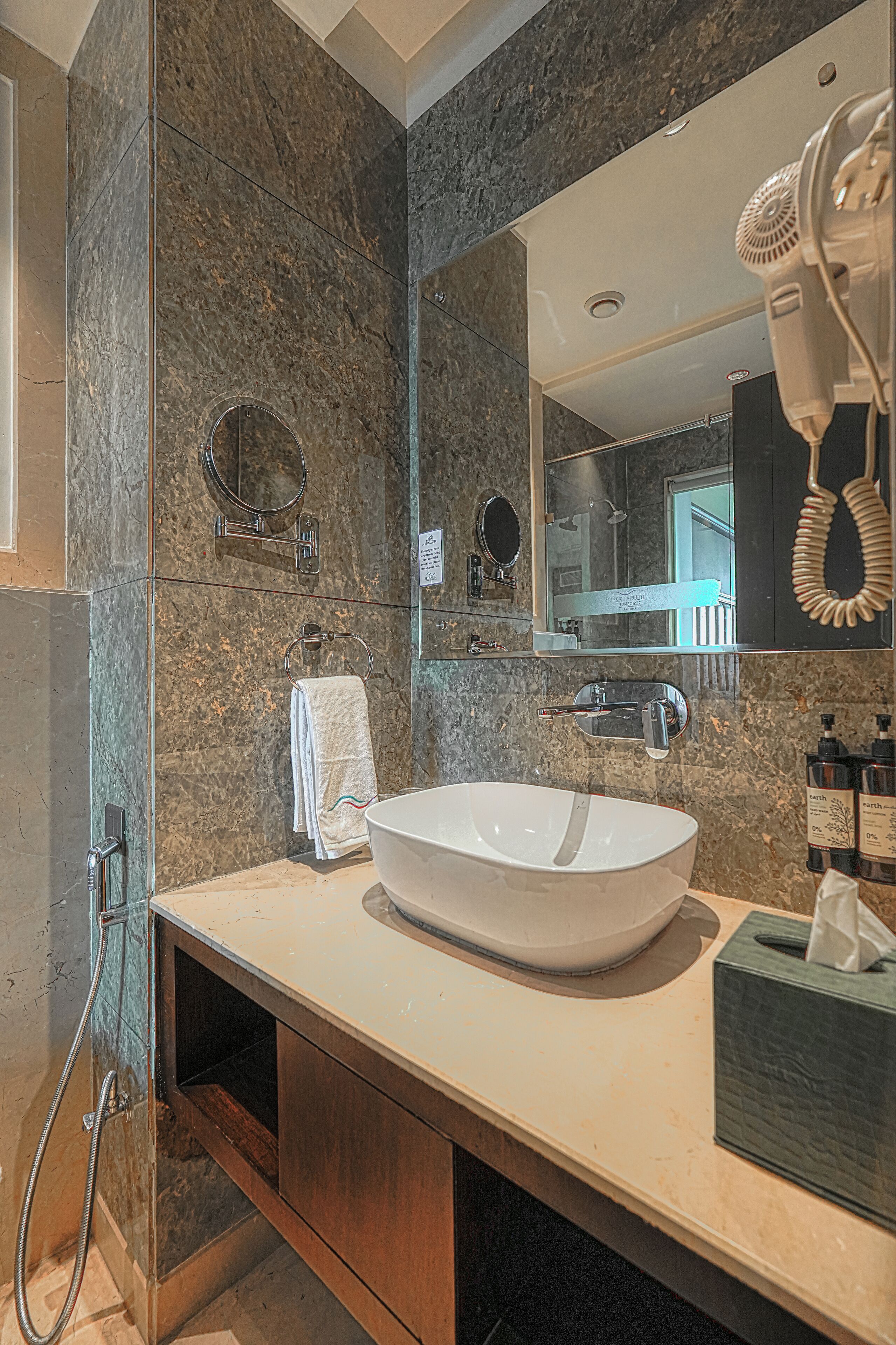 Une salle de bain moderne avec un grand miroir, un lavabo blanc et un sèche-cheveux posé sur le comptoir.