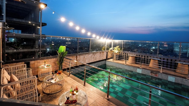 Zona de piscina en la azotea con barandilla de cristal, mobiliario de mimbre e iluminación con luces colgantes.