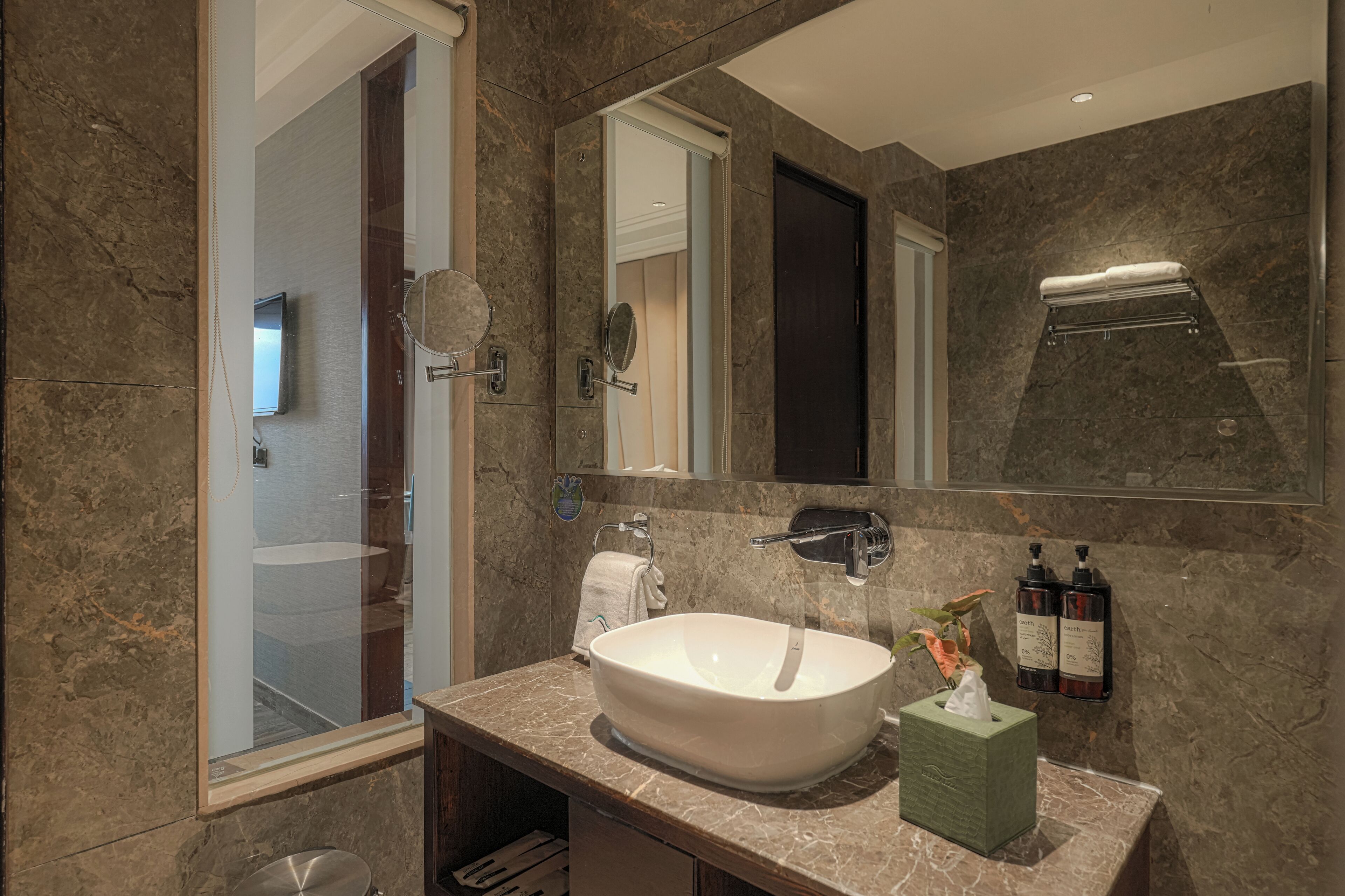 Un baño moderno con un lavamanos ovalado grande, un espejo, un perchero para toallas y dos botellas de jabón de manos.