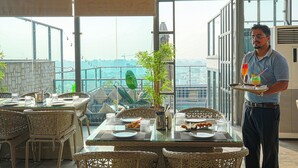 Comedor con mobiliario de mimbre, una mesa de vidrio y vistas de la ciudad a través de amplias ventanas.
