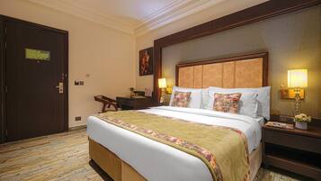 Una habitación de hotel con una cama grande, dos mesitas de noche con lámparas, un escritorio y una silla.