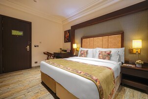 Una habitación de hotel con una cama grande, dos mesitas de noche con lámparas, un escritorio y una silla.