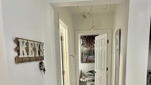 A hallway with a dark blue rug, a 'KEYS' sign, and a door leading to a room with a beach-themed painting. - Super Spacious 3 Bedroom House, w/2 Living Rooms and Close to Everything  (Shreveport)