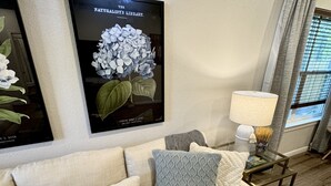 Una sala de estar con un sofá color beige, una manta con estampado y una impresión botánica enmarcada en la pared.