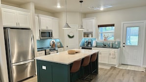 Una cocina moderna con armarios blancos, electrodomésticos de acero inoxidable, una isla central con taburetes y vistas al exterior.