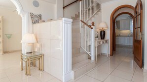Una escalera con barandillas blancas y un pasamanos de madera que lleva a una zona de cocina.