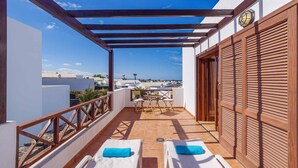 A balcony with two sunbeds, a table, and chairs, overlooking a cityscape. - Villa Rioja - Three Bedroom Villa, Sleeps 6 (Playa Blanca)