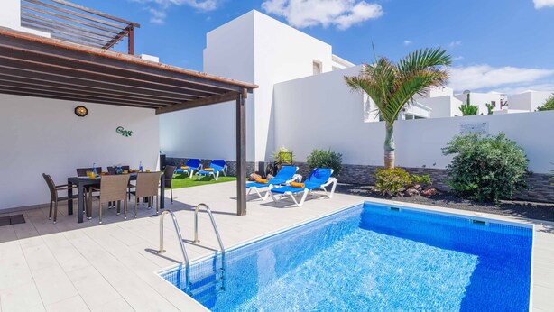 A swimming pool with lounge chairs, a table with chairs, and a pergola. - Villa Rioja - Three Bedroom Villa, Sleeps 6 (Playa Blanca)
