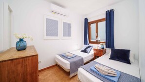 A bedroom with two beds, a wooden desk, an air conditioner, and a window with curtains. - Villa Rioja - Three Bedroom Villa, Sleeps 6 (Playa Blanca)