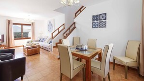 A spacious living area with a wooden dining table, beige chairs, a sofa, and a staircase. - Villa Rioja - Three Bedroom Villa, Sleeps 6 (Playa Blanca)
