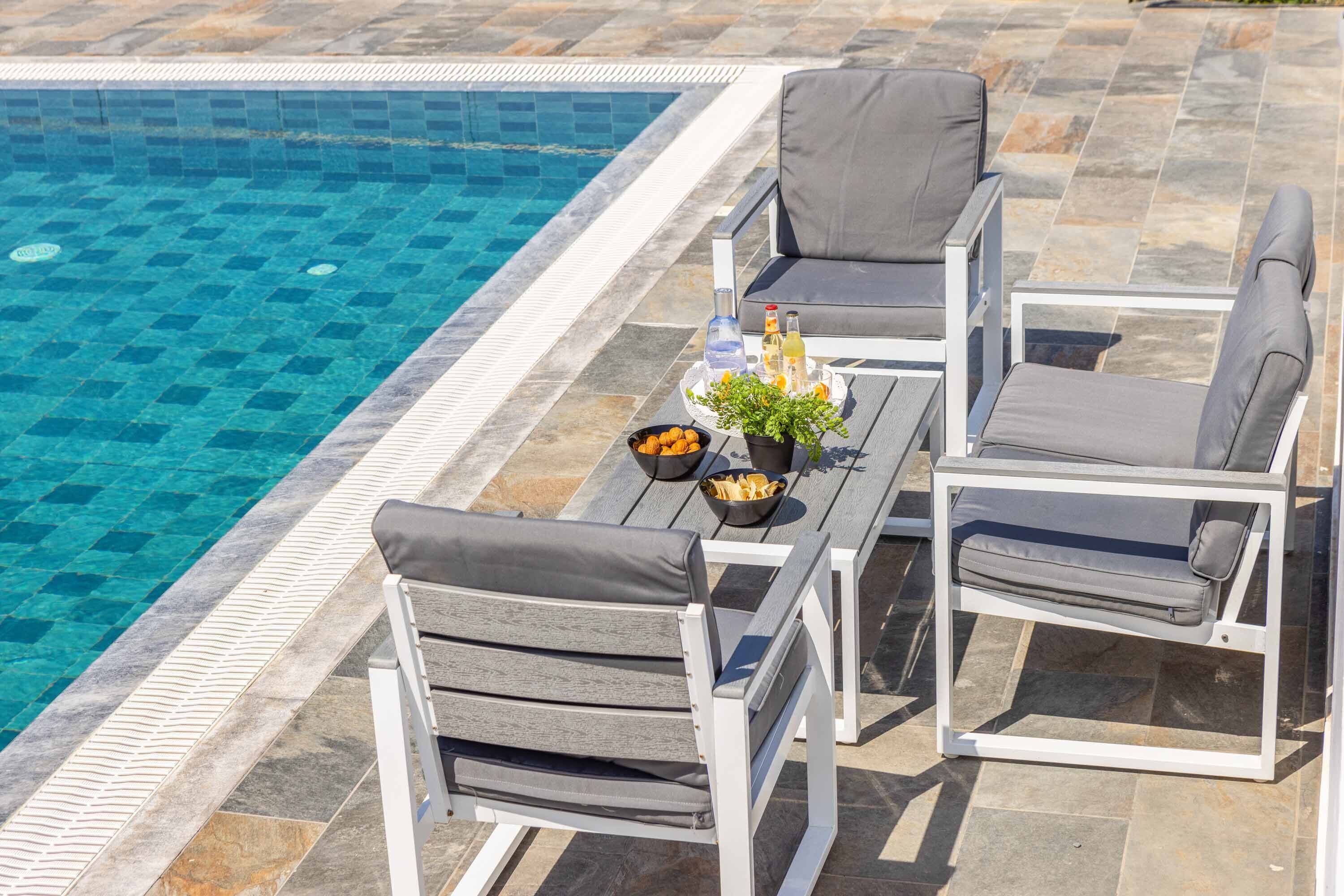 A poolside area with a table, chairs, and a tray with drinks and snacks.
