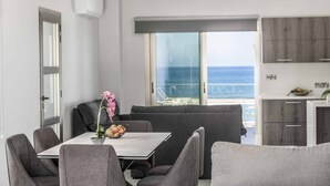 Un comedor moderno con una mesa y sillas, vista al océano a través de un ventanal grande, y una cocina con armarios de madera.