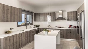 Una cocina moderna con una isla central, armarios de madera, electrodomésticos de acero inoxidable y vistas al mar a través de un ventanal.