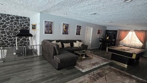 A living room with a stone wall, a dark sofa, a pool table, and a patterned rug.