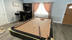 A pool table with a cue stick, a dog bed, a bar area, and a 'Blessed' sign on the wall.
