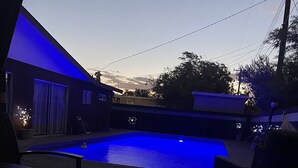 A swimming pool with blue lighting, surrounded by outdoor furniture and a building with a garage.