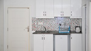 A compact kitchen with white cabinets, a small refrigerator, and a tiled backsplash. - Damla Suit Otel (Gaziantep)