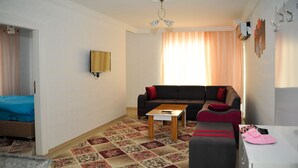 A living room with a sofa, ottoman, coffee table, and a small white table. - Damla Suit Otel (Gaziantep)