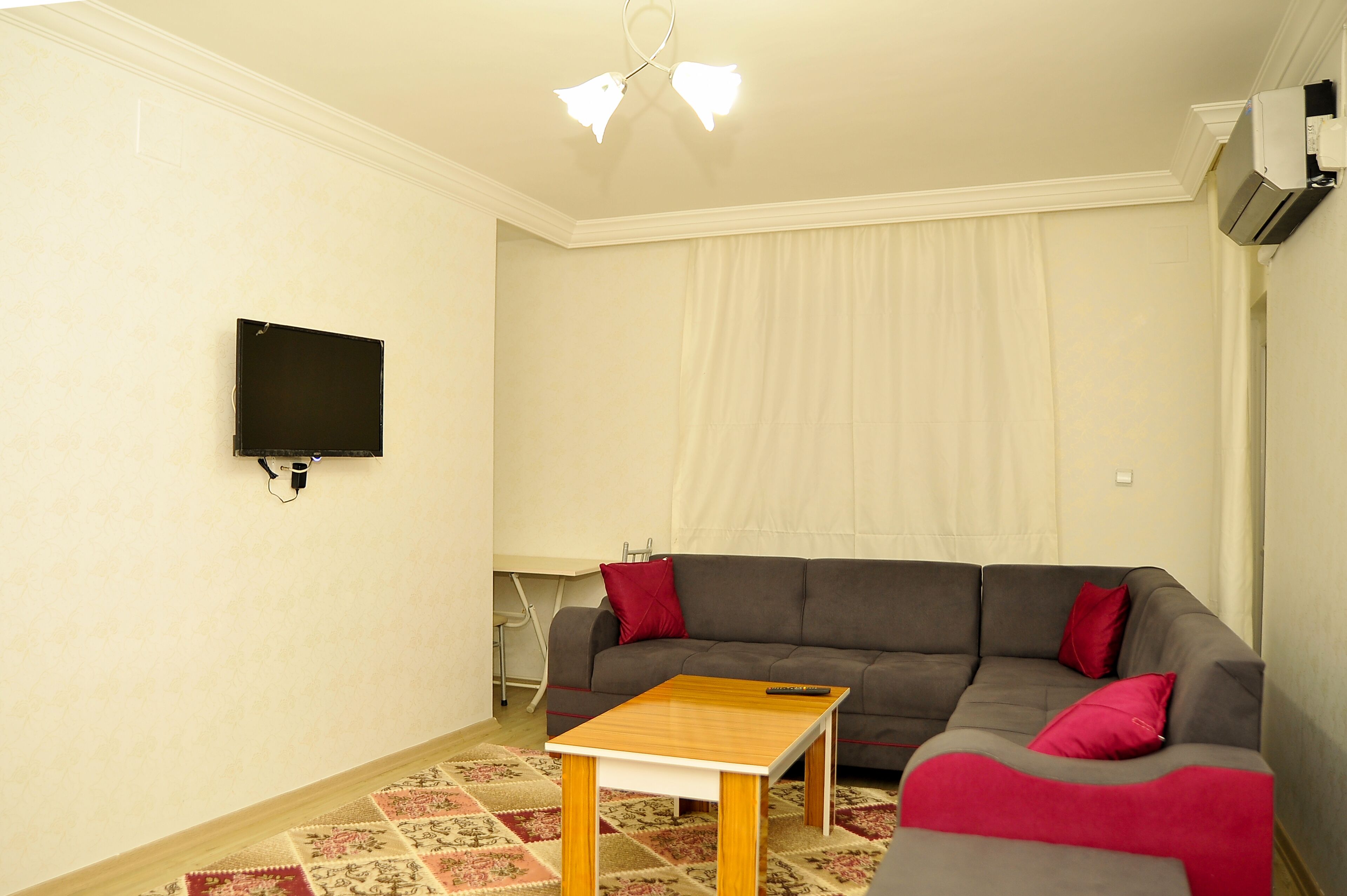 A living room with a grey sofa, a wooden coffee table, a flat-screen TV mounted on the wall, and a patterned rug.