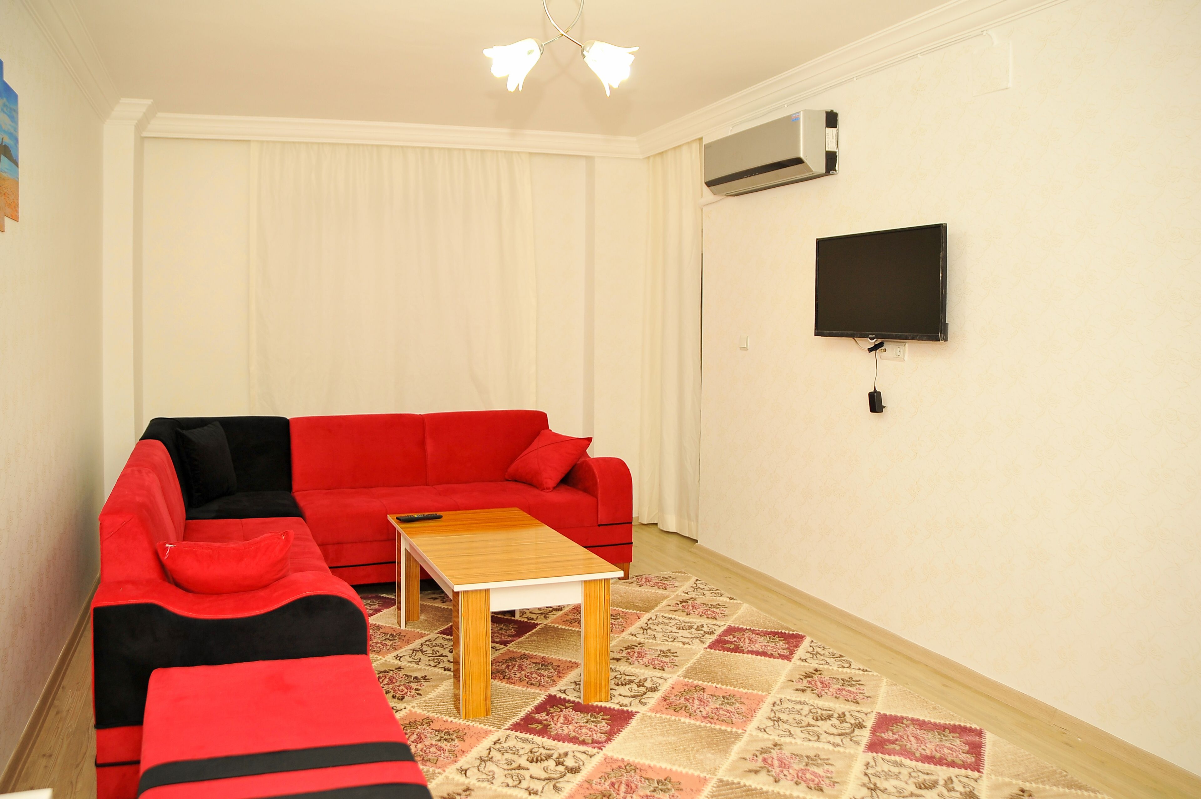 A living room with a red sofa, a wooden coffee table, and a flat-screen TV mounted on the wall.