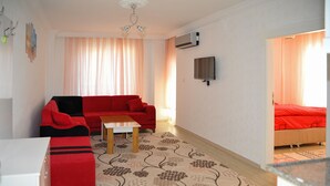 A room with a red sofa, a small table, a patterned rug, and a bed with a red cover. - Damla Suit Otel (Gaziantep)