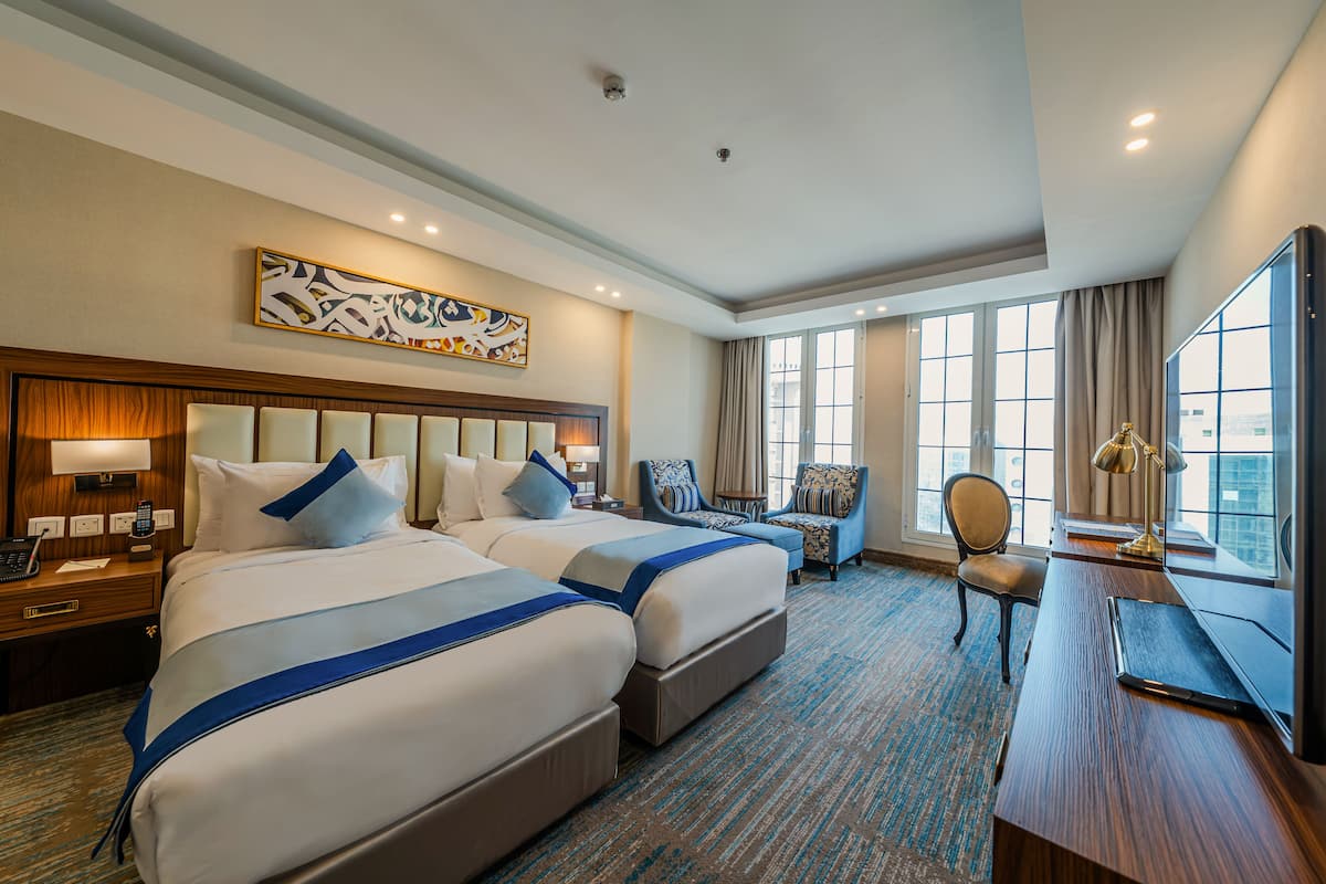 A hotel room with two beds, a desk, a chair, and a large window.