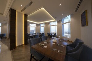 Ein moderner Essbereich mit einem langen Tisch, der für eine Mahlzeit gedeckt ist, großen Fenstern mit Rundbögen und Blick auf die Stadt.