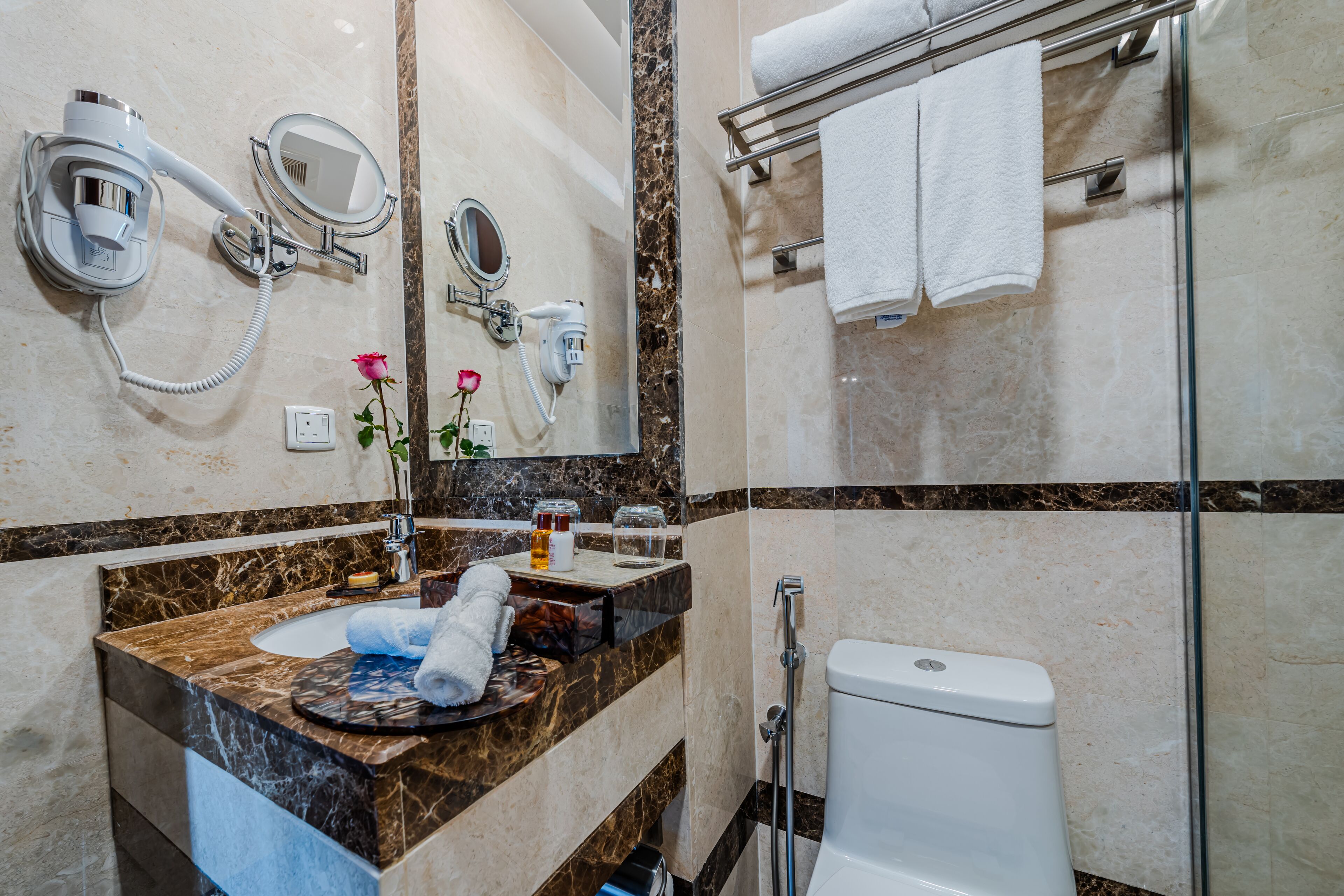 A bathroom with a marble sink, a hairdryer, a mirror, a towel rack, and a toilet.