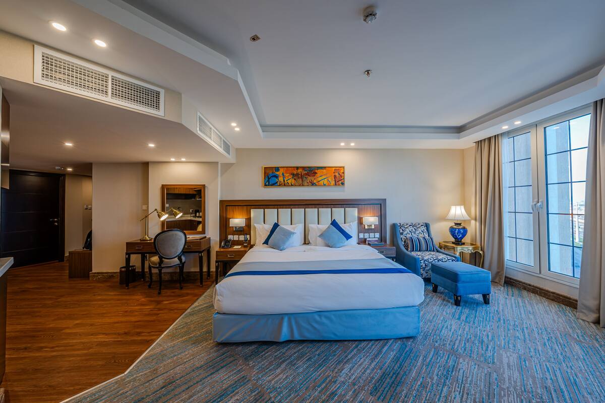 A hotel room with a large bed, a desk, a chair, a small table, and a window with curtains.