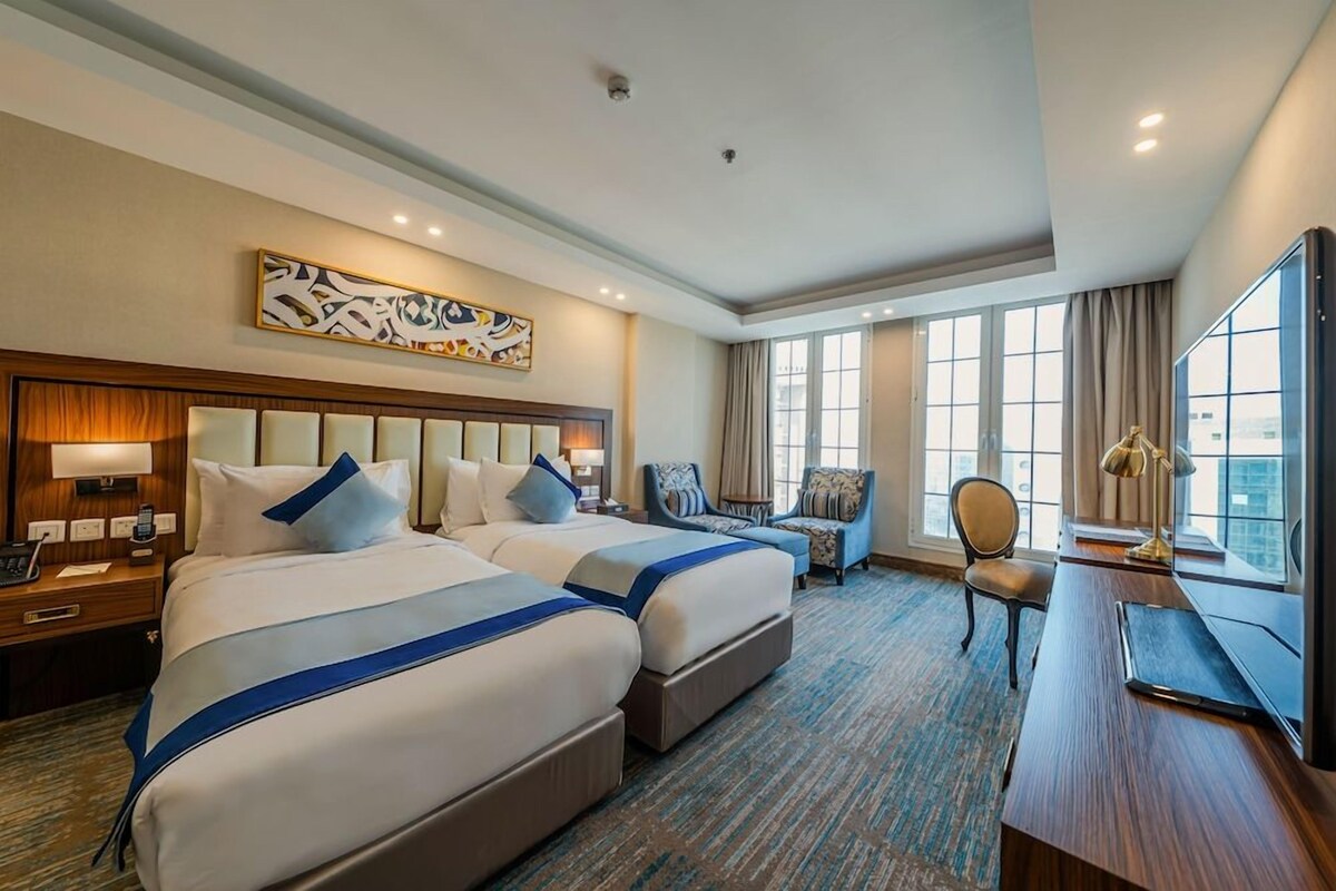 A hotel room with two beds, a desk, a chair, and a large window.
