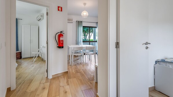 A hallway leading to a dining area with a fire extinguisher mounted on the wall, a white table, and chairs.